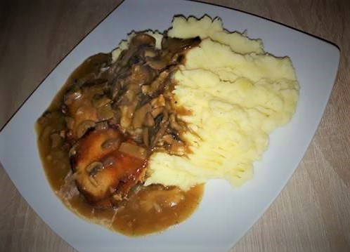 A plate with mashed potatoes and meat topped with onion and red wine gravy.