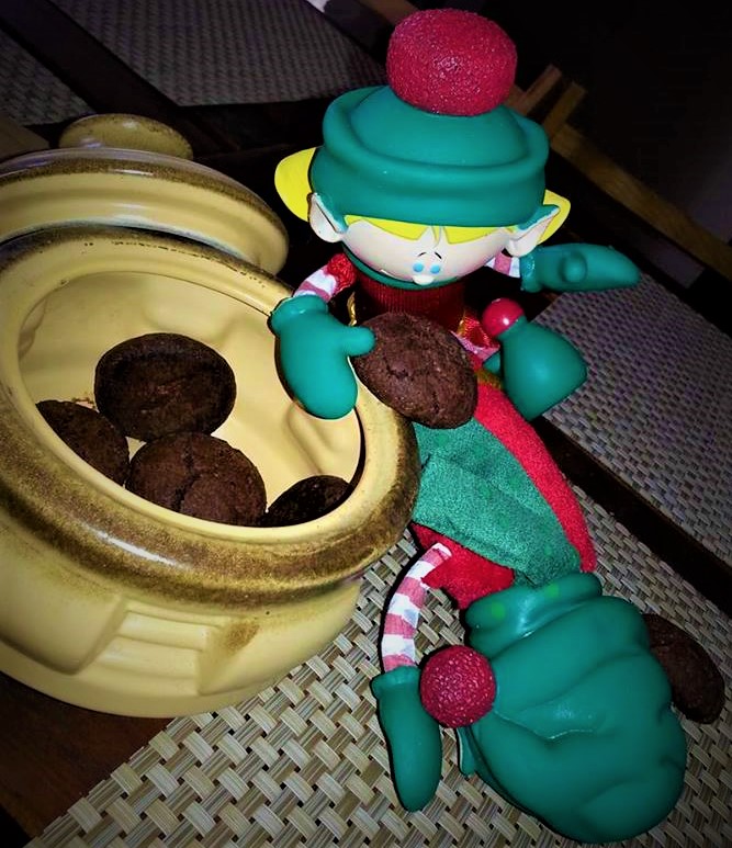 A toy elf sitting next to a bowl of cookies.