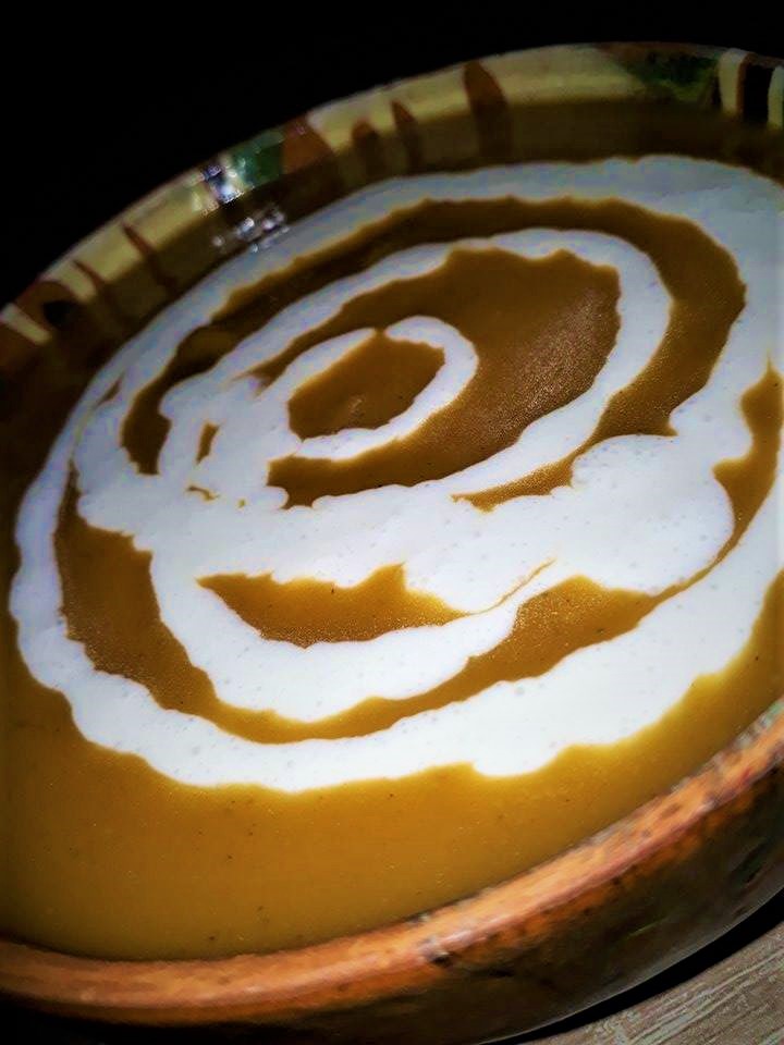 A bowl of squash soup with a swirl of cream on top.