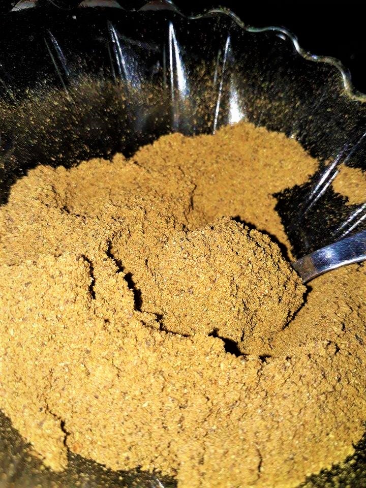 A bowl of brown powder with a spoon in it, containing garam masala.