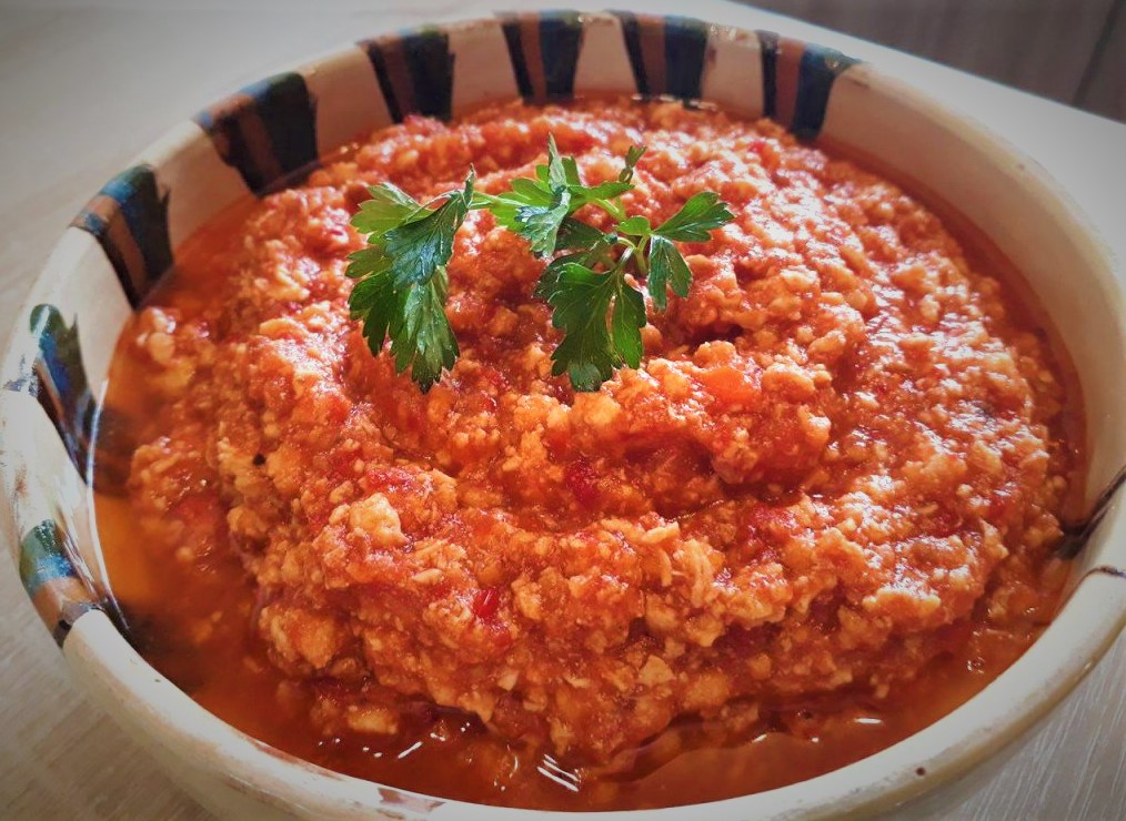 A bowl of hummus with tomatoes and parsley, topped with chicken ragu.