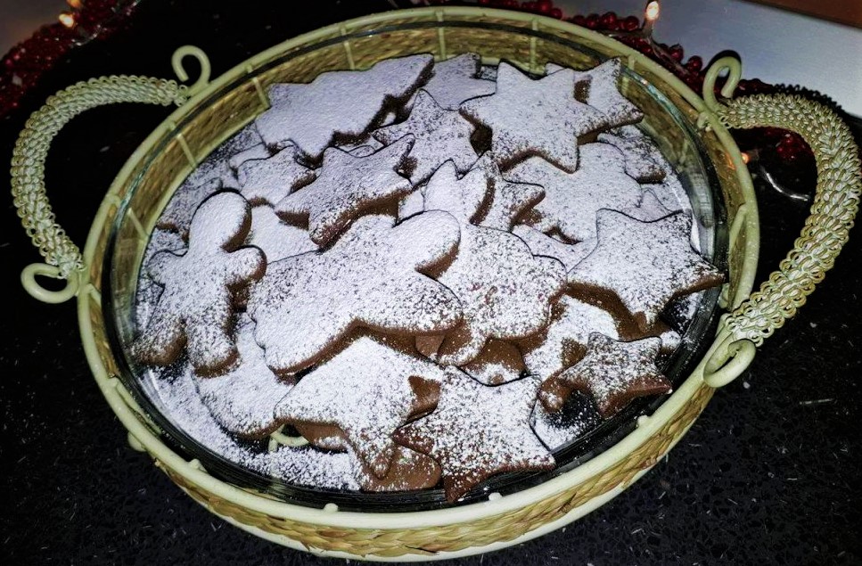 A wicker basket filled with gingerbread cookies and powdered sugar.