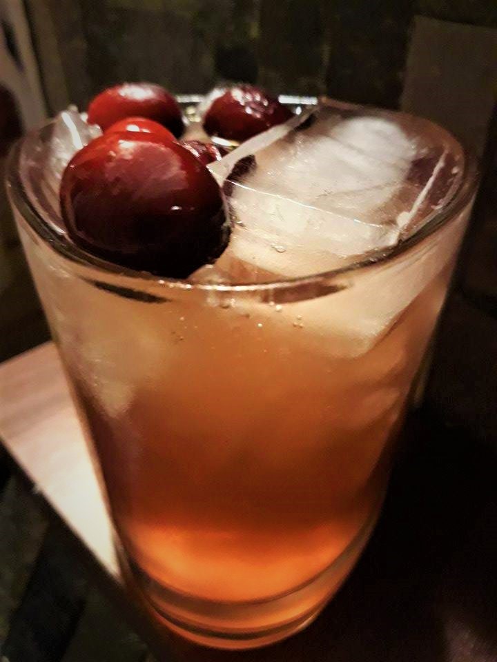 A cocktail recipe with cherries and ice served in a glass.