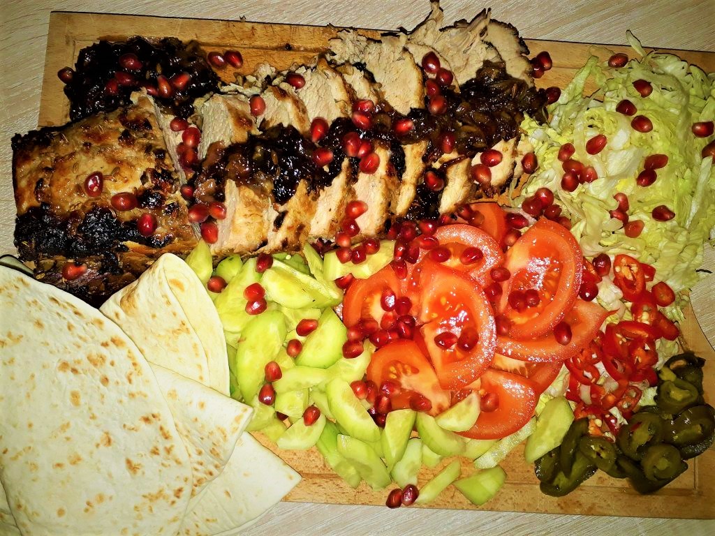 A wooden cutting board with meat, vegetables, and tortillas.