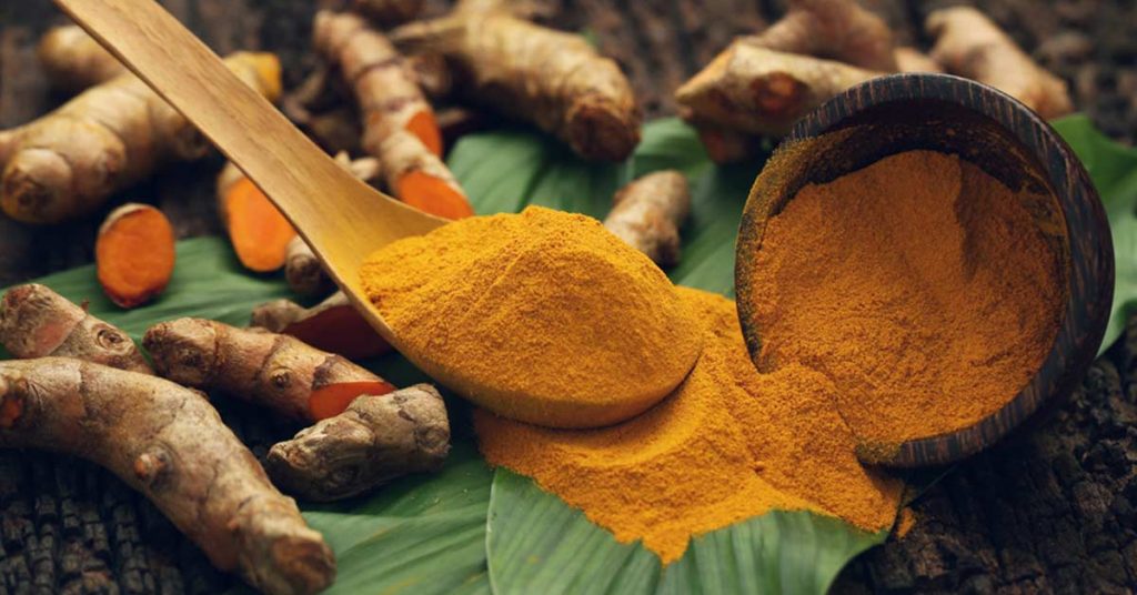 Tumeric powder and leaves on a wooden spoon.