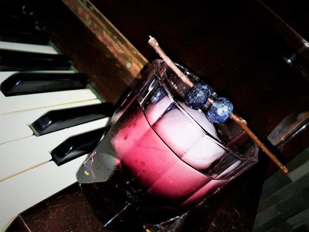 A drink with blueberries on top of a piano keyboard.