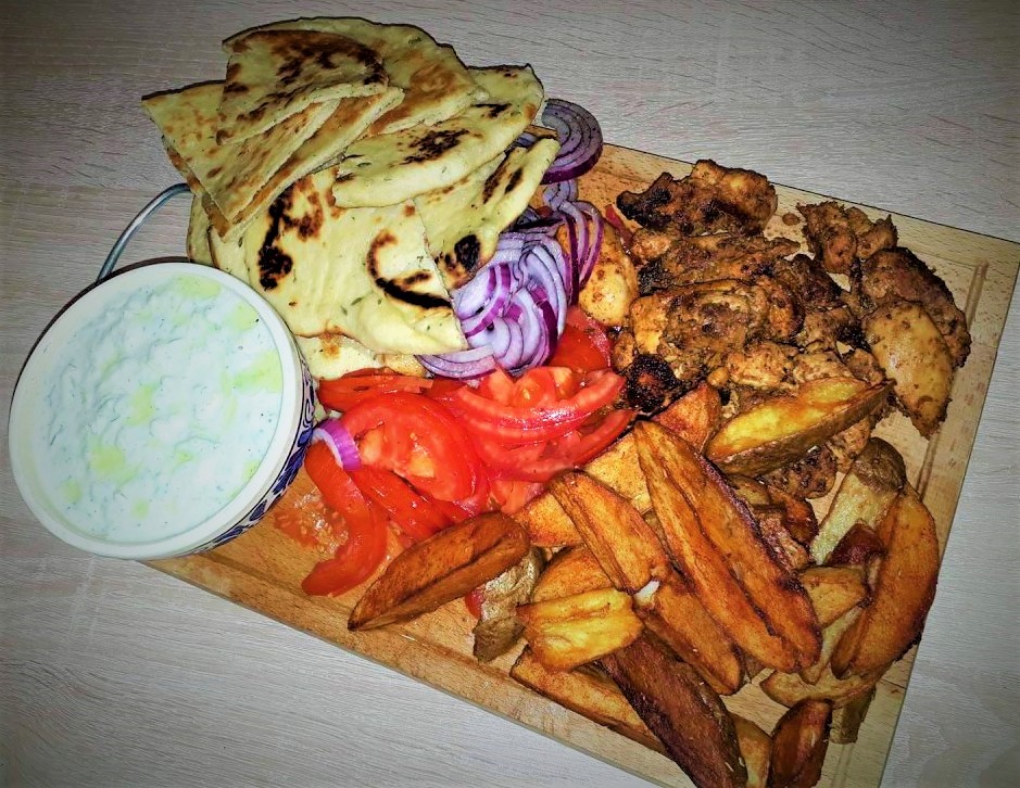 A wooden cutting board with chicken, fries and dip.