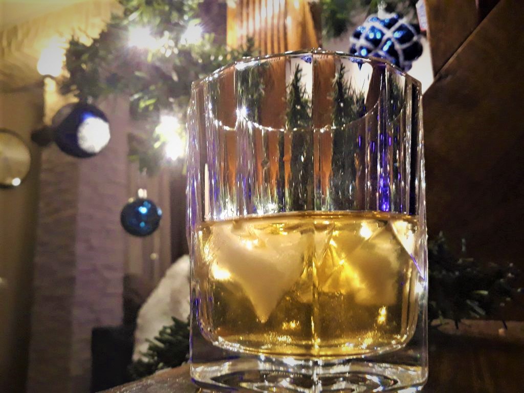 A glass of whiskey sitting on a table in front of a christmas tree.