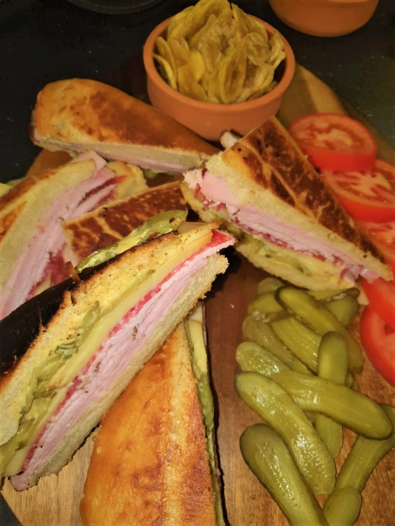 A plate of sandwiches and pickles on a wooden cutting board.